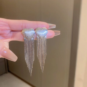 Detail of silver heart tassel earrings with brushed texture held in hand for scale