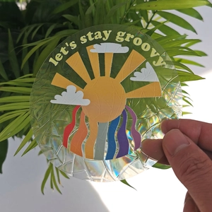 Detail of round holographic suncatcher sticker featuring sun, clouds and groovy text