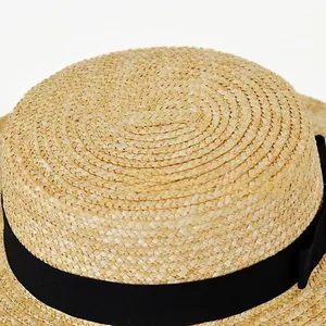 Detailed top view of the tight weave texture on a flat-top straw boater hat with black ribbon