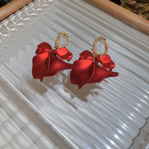 Macro detail of red rose petal drop earrings on a textured glass display tray