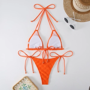 Flat lay of orange bikini with textured waffle pattern next to beach accessories