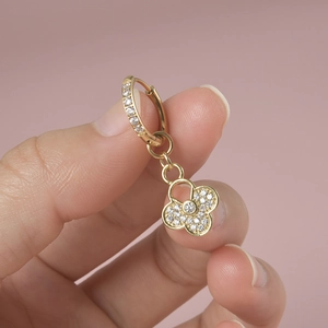 Close-up of gold clover drop earrings with white crystal pave setting held by fingers