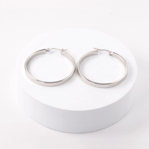 Detailed close-up of polished silver stainless steel hoop earrings on a white stand