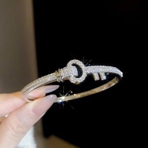 Close-up of silver key-shaped bracelet with cubic zirconia paving held by a hand