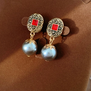 Detailaufnahme der Vintage-Ohrringe mit rotem Edelstein und grauer Perle auf Samt