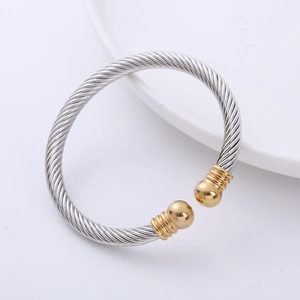 Polished silver cable wire cuff bracelet with gold ball ends on a white background
