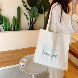 Détail de la broderie beloved sur un sac cabas en toile crème porté par un mannequin