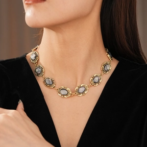 Detail of vintage gold necklace with grey oval resin gemstone worn by a fashion model