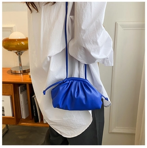 Detail of bright blue pleated cloud pouch bag worn over shoulder with white shirt