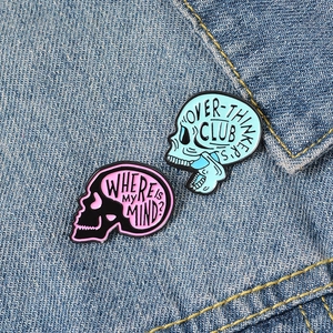 Punk style skull enamel pins on denim with 'Over-thinker's club' text in black and blue
