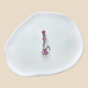 Close-up of a silver bunny belly ring with pink heart-shaped crystals on a white ceramic plate