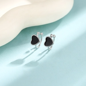 Macro shot of silver metal heart ear clips with black enamel inlay on blue background
