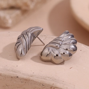 Macro shot of silver pleated wing earrings on a textured stone base highlighting polished metal