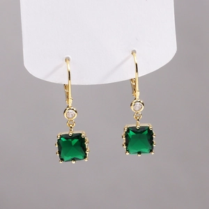 Détail de boucles d'oreilles dorées 18K avec zircons verts de taille émeraude