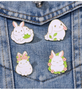 Close-up of four white rabbit enamel pins with sakura flowers on denim fabric