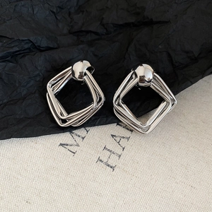 Macro shot of silver geometric square layered metal stud earrings on a textured background