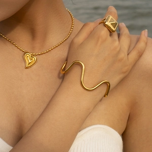 Macro view of 18k gold plated wave bracelet and heart necklace set on female model