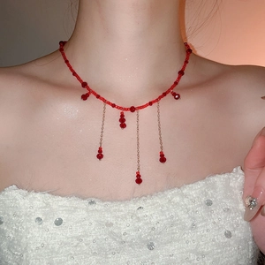 Detail of red crystal beaded necklace with golden tassels on a white textured sweater