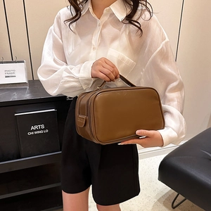 Brown leather toiletry bag with top handle and double zipper shown in a modern interior