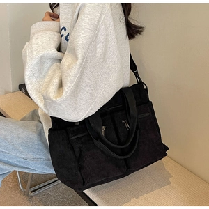 Close-up of black corduroy tote bag featuring multiple zipper pockets and texture detail