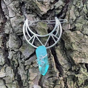 Detailed view of silver moon hair clip with blue crystal on a rustic bark background