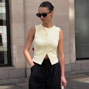 Détails de la maille côtelée jaune pâle du gilet sans manches boutonné sous lumière naturelle