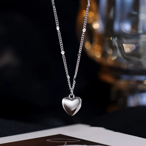 Macro shot of a silver heart pendant necklace with fine bead chain on dark elegant background