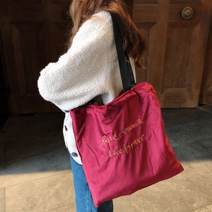 Detail of burgundy velvet tote bag with gold love rewards the brave embroidery