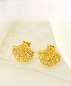 Detailed view of gold shell earrings with inlaid zircons on soft white silk fabric