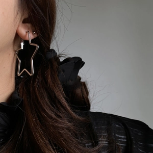 Close-up of a silver star-shaped hoop earring worn by a model in a minimalist style