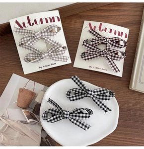 Detailed view of three pairs of plaid bow hair clips in black, brown, and grey on a display card