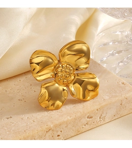 Detailed macro view of an 18K gold plated clover ring on a beige textured stone base