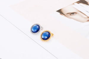Detailed shot of round crystal stud earrings in gold and silver with deep blue stones