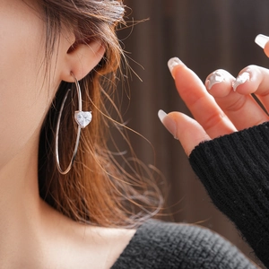 Gros plan d'une créole en C argentée avec zircon en forme de cœur sur l'oreille du mannequin