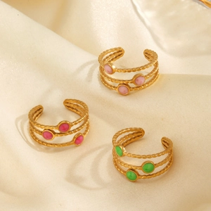 Three-layer wave gold rings with pink red and green stone accents on beige silk