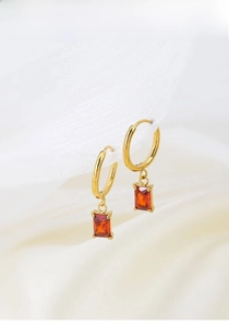 Detailed macro view of gold hoop earrings with square red zircon stone on white silk