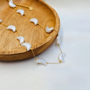 Macro detail of a gold necklace with white crescent moon pendants on silk and wood