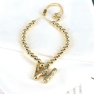Detail of adjustable gold beaded bracelet featuring a shimmering letter W zircon charm