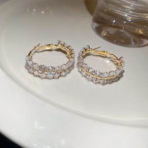 Gros plan de boucles d'oreilles créoles dorées avec zircons étincelants sur assiette blanche