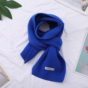 Detail view of a blue knitted winter scarf with brand tag on a soft white background