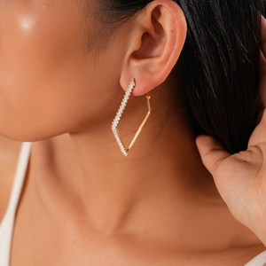 Macro side view of a geometric gold earring with diamond accents on a model's ear