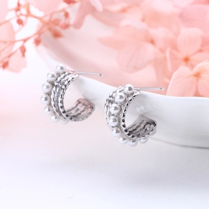 Macro view of C-shaped silver earrings with twisted metal and white pearl inlay