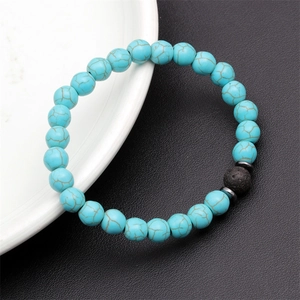 Detail of blue turquoise beaded bracelet with black lava stone on white ceramic plate