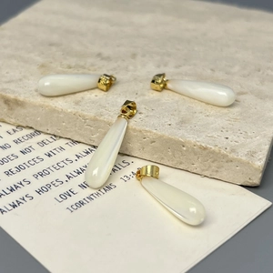 Cuatro colgantes de nácar blanco en forma de gota con aros dorados sobre piedra beige