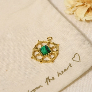 Close-up of gold pendant with green malachite stone on rustic linen packaging bag