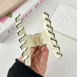 Elegant off-white pearl claw clip with black wave edge held by hand on white background