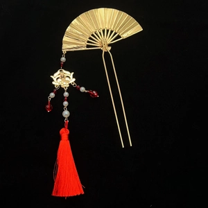 Detailed view of golden fan hair pin with red silk tassels and beaded accents on black