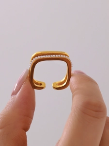 Detail of a square gold open ring with small white pearls on a minimalist finger display