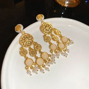 Détail de boucles d'oreilles rétro dorées à glands de perles avec pierres blanches sur plat