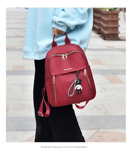 Detail view of burgundy oxford cloth backpack with golden zippers and a cute panda pendant